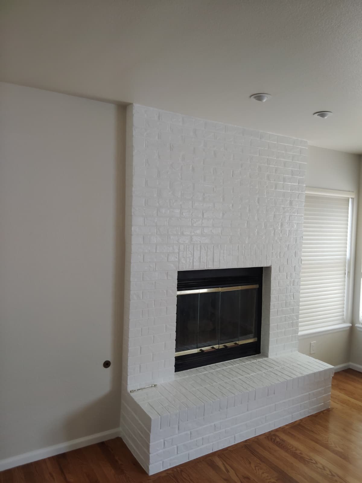 Refinished brick fireplace painted crisp white with clean trim and tidy hardwood floors